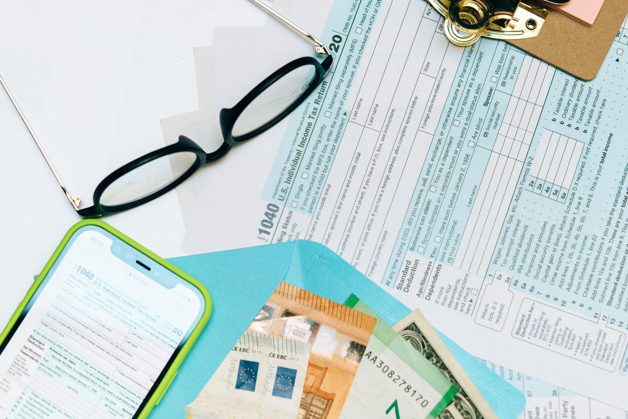 Close-up of tax forms, smartphone, and dollar bills for financial analysis and preparation.